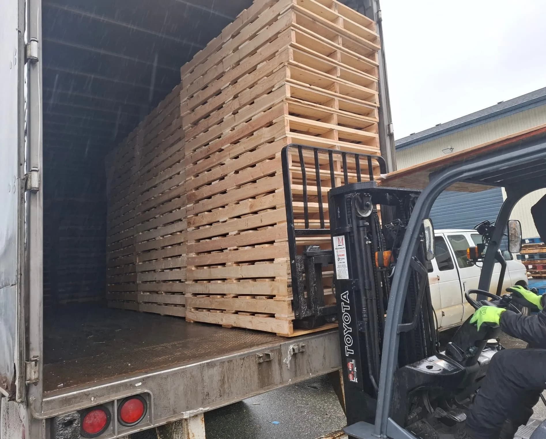 Forklift loading stacked wooden pallets into truck in the rain